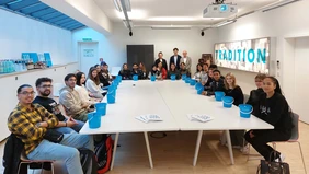 A group of young people sit around a large conference table, each with a blue bucket in front of them.