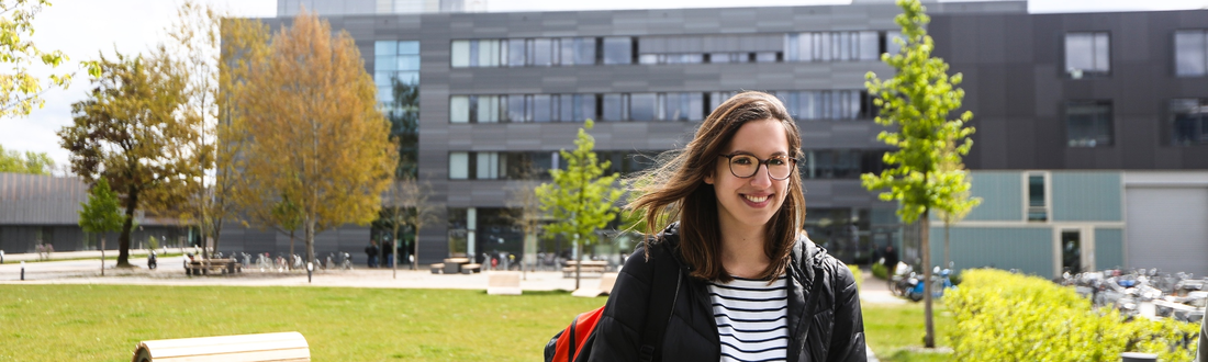 Studentin vor Campuswiese, Gebäude G im Hintergrund