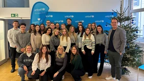 A group of young people in front of a blue UNICEF-branded wall next to a Christmas tree decorated in blue.