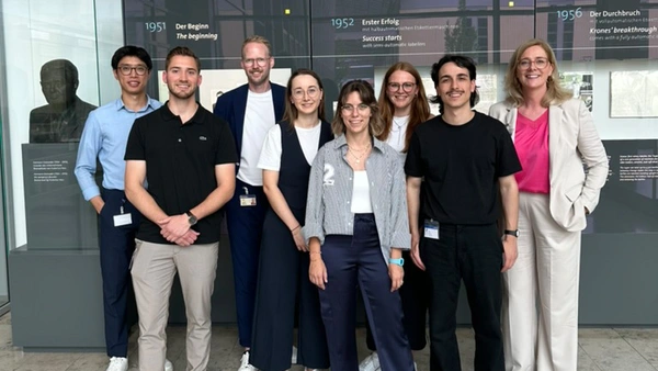 A group of people in the Krones AG company building, with a display wall about the company's history in the background.