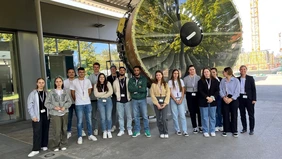 A group of people in front of a giant turbine and a company building.