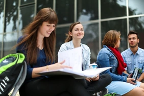 [Translate to English:] Studierende der Fakultät sitzen vor der Tür auf den Steinen