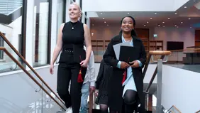 Zwei junge Frauen auf einem Treppenaufgang im Gebäude, frontal aufgenommen